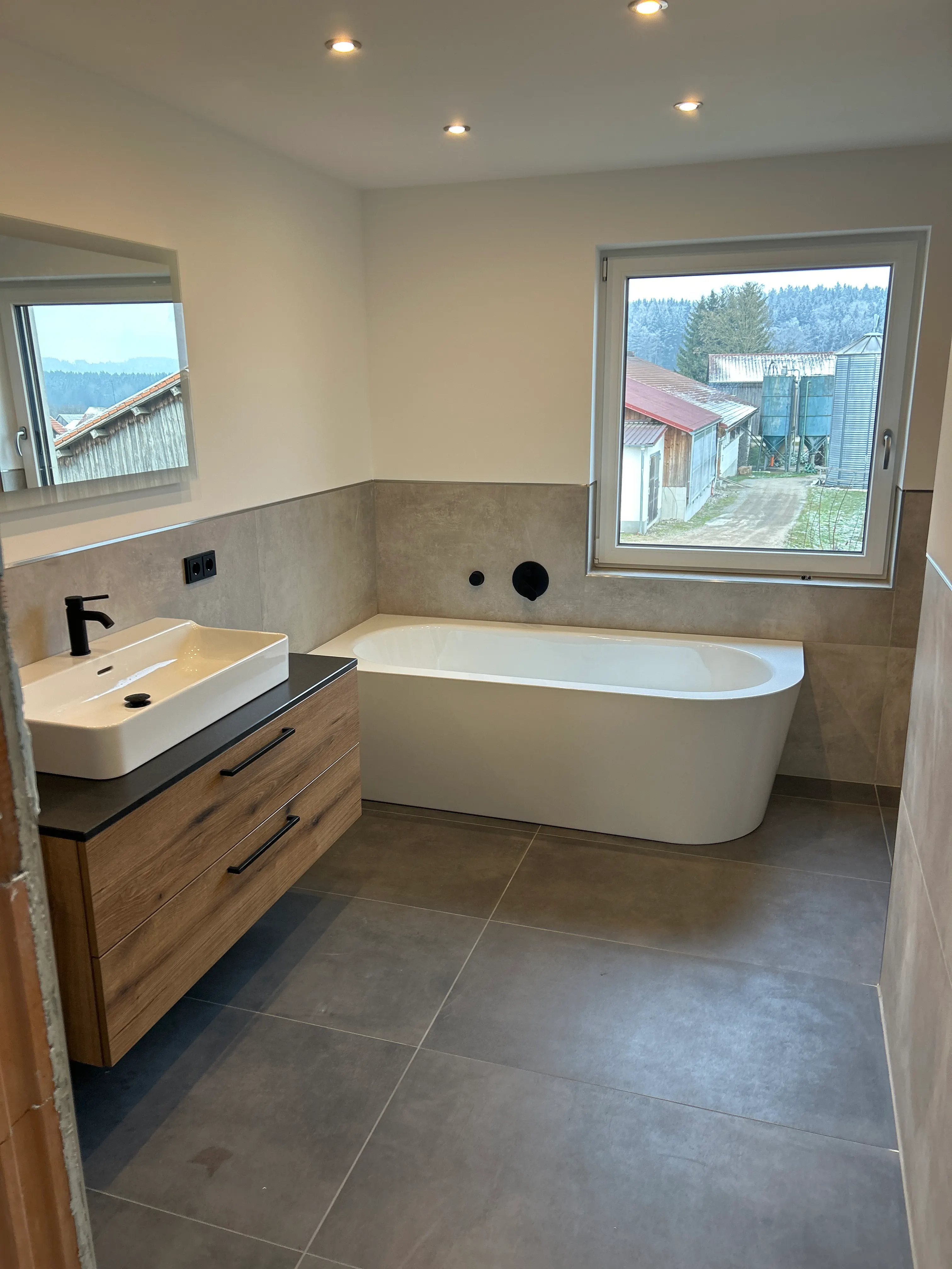 Frisch sanierte Badezimmer mit moderner Badewanne, Waschtisch in Holz-Optik und großformatigen Fliesen.