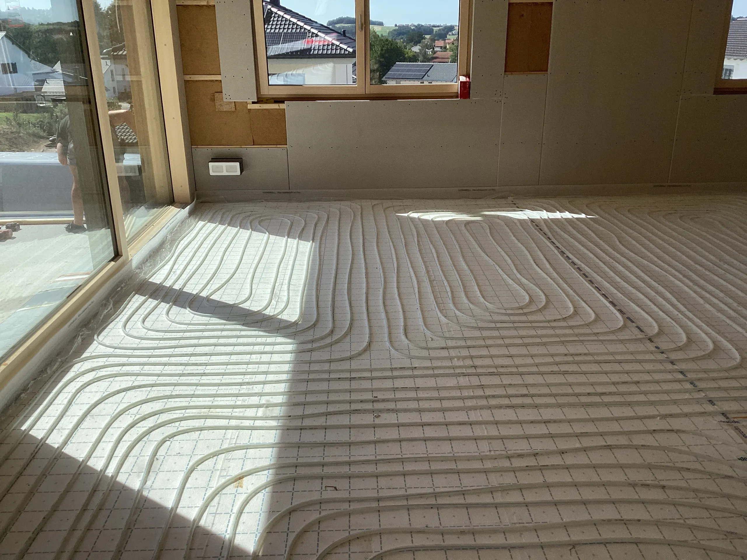 Verlegte Fußbodenheizung mit Heizrohren auf Dämmplatten in einem Neubau-Wohnraum mit Blick ins Grüne.