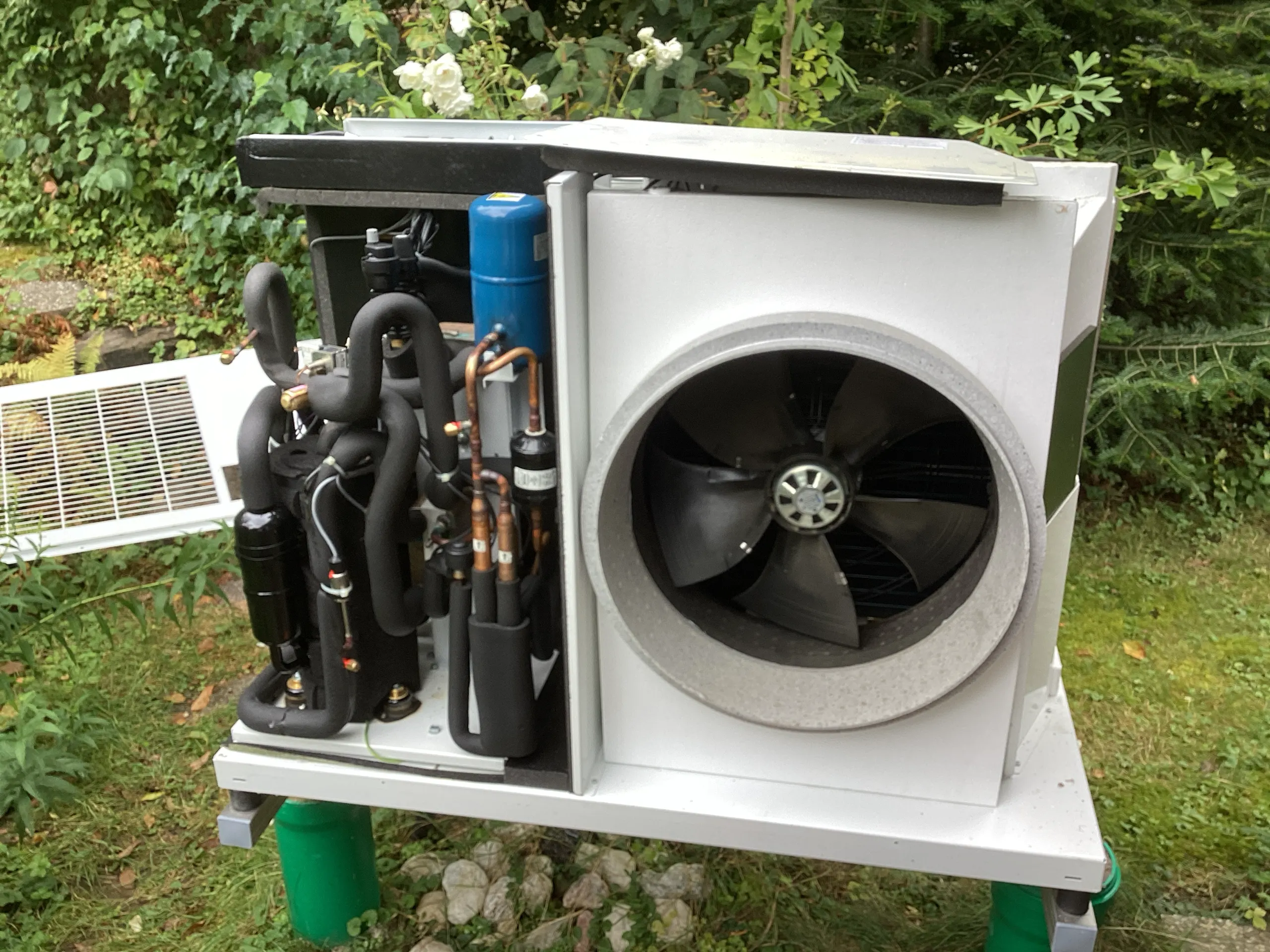 Wärmepumpen-Außengerät mit geöffneter Abdeckung im Service-Einsatz: Verdichter, Kältekreis und Lüfterrad sichtbar.